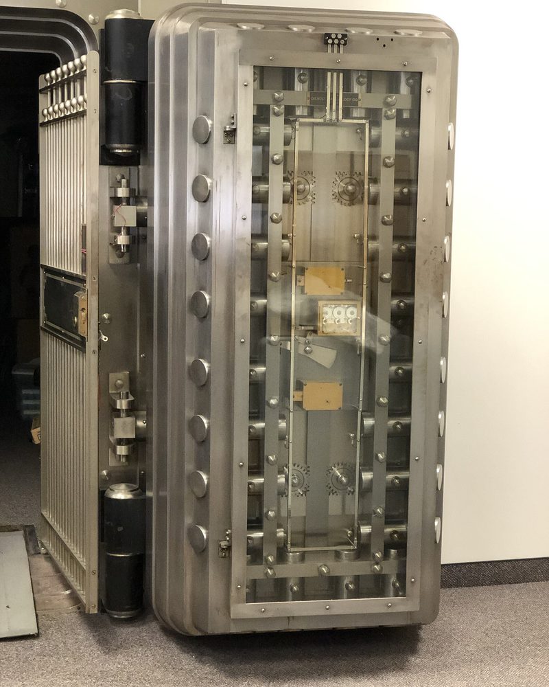 An open bank vault door swung back on its hinge, the steel locking bolts and gearing exposed across its inner face