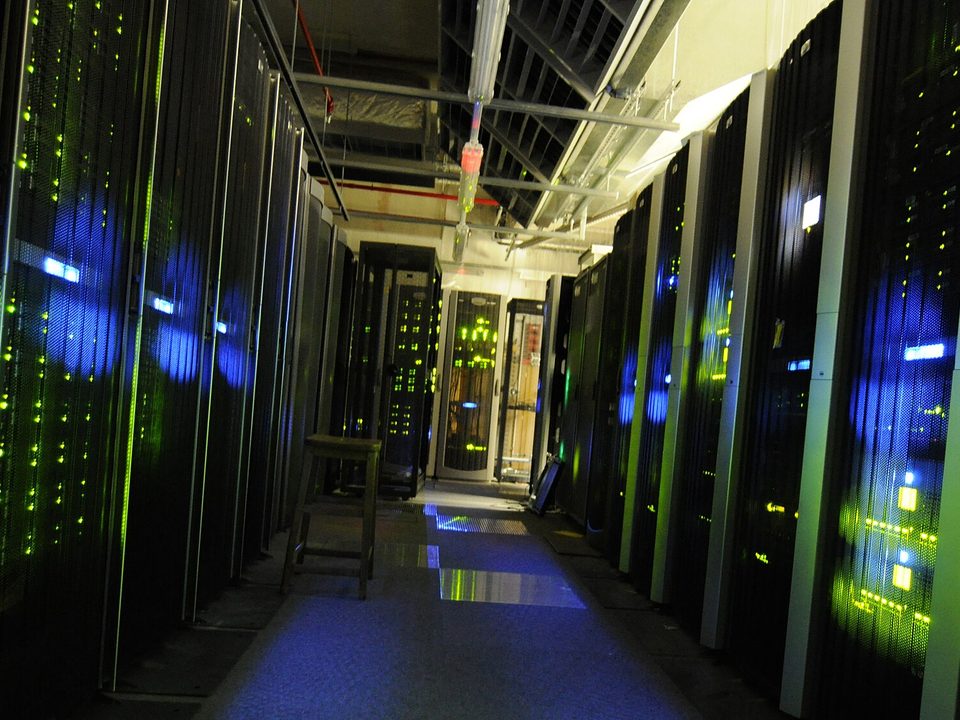 A narrow aisle between two rows of server cabinets, indicator lights running the length of both racks