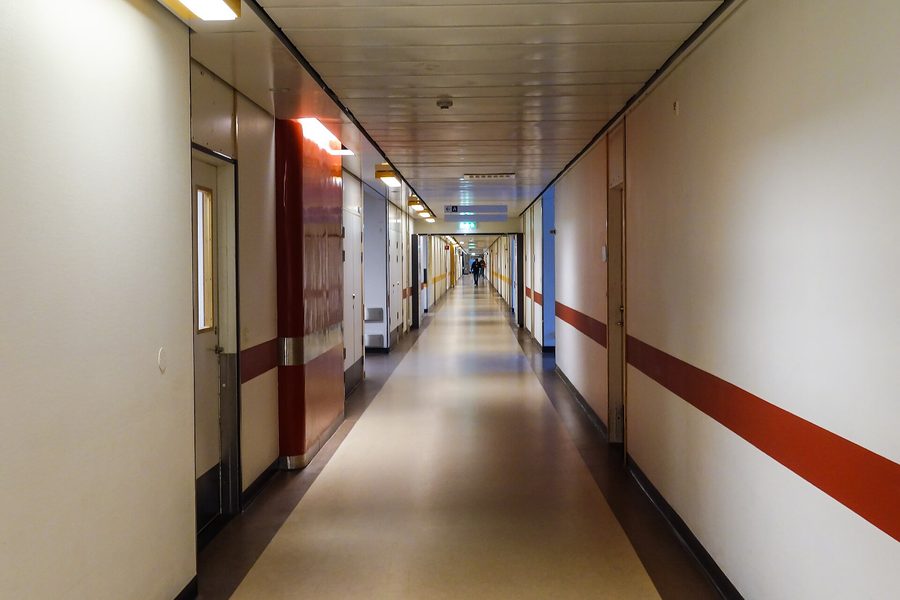 A long hospital corridor with a red wayfinding band running along the wall and a single figure at the far end
