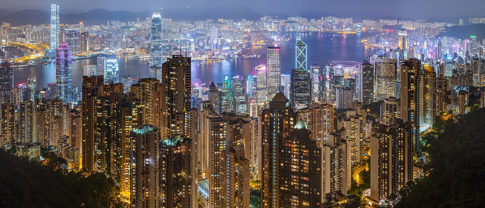Hong Kong harbour at night, the lit towers of the central business district massed across the water below a wooded ridge