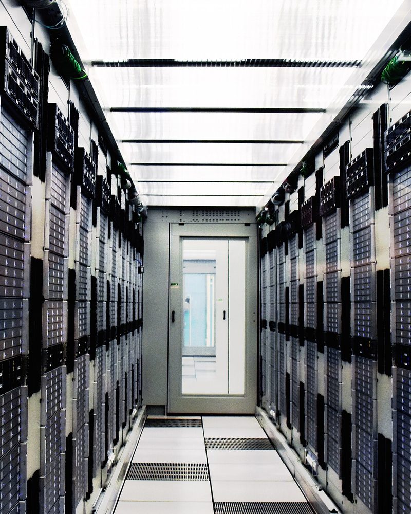 A long symmetric aisle between two rows of floor to ceiling server cabinets in the CERN computer centre, a glazed door closing the far end