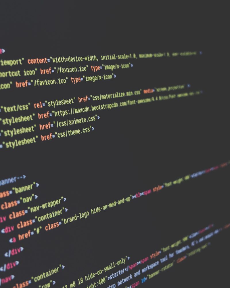 A monitor photographed at a steep angle showing lines of HTML and CSS markup in a dark editor theme